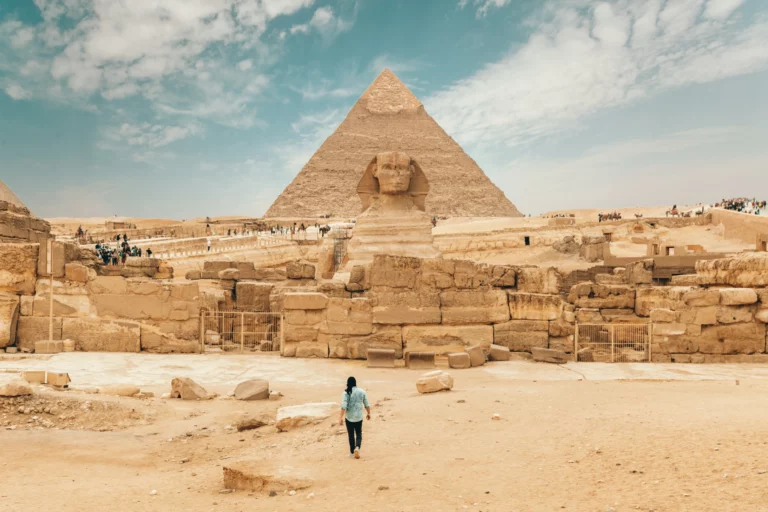 A person walking away from the camera in front of the sphynx and pyramid in Egypt