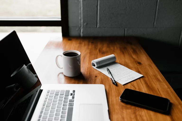 A laptop, cup of coffee, notebook and phone on a table